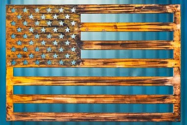American Flag Metal Art wall decor depicting an American Flag cut out of metal. Picture shows a Wood Grain Copper Patina finish.