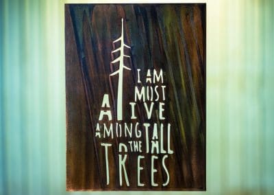 I Am Most Alive Among The Tall Trees metal wall art is a metal sign with the saying cut into the metal. This piece has a Camo Patina finish.
