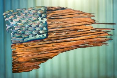 Battled Colors is metal wall art design depicting a tattered American Flag made out of metal. This particular flag has a multi-color patina which highlights the area around the cut out stars blue while the stripes are a deep woodgrain copper look.