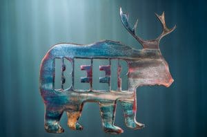 Metal art of a bear body with deer antlers and the word "beer" in the body of the bear - all cut out of metal. This piece has a multi-color patina finish with dark blues and purples throughout the body of the bear.