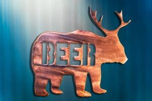 Metal art of a bear body with deer antlers and the word "beer" in the body of the bear - all cut out of metal. This piece has a wood grain copper patina.