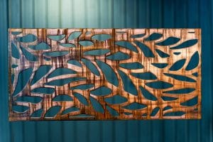 Metal wall art screen with long leaf pattern cut out of metal on wood grain copper patina finish
