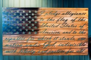 The American Flag metal wall decor with the Pledge of Allegiance cut into the metal. The metal is hand finished and has been coated with a multicolor patina to highlight the blue around the stars and woodgrain for the stripes.