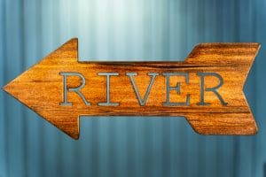 Metal wall art of River directional sign - Left facing - with metal shaped arrow with Lake cut into the middle. This piece has a wood grain copper patina finish.