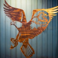 Metal wall art of American Bald Eagle with expanded wings and fish in talons all cut out of metal with a Wood Grain Copper Patina. There is also a portrait of a bald eagle in the right week cut out of metal.