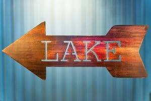 Metal wall art of Lake directional sign - Left facing - with metal shaped arrow with Lake cut into the middle. This piece has a wood grain copper patina finish.