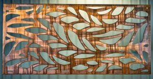Metal wall art screen with long leaf pattern cut out of metal on wood grain copper patina finish