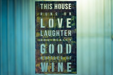 Metal wall art sign saying This House Runs on Love, Laughter and Really Good Bottles of Wine