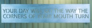 Metal wall art with Your Day Will Go The Way the Corners of Your Mouth Turn saying cut into metal