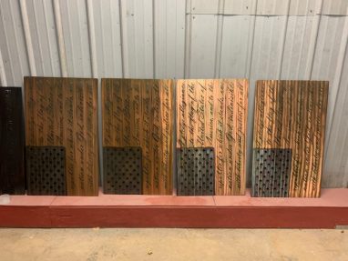 The American Flag metal wall decor with the Pledge of Allegiance cut into the metal. The metal is hand finished and has been coated with a multicolor patina to highlight the blue around the stars and woodgrain for the stripes. This picture shows four Pledge Flags lined up at the shop.
