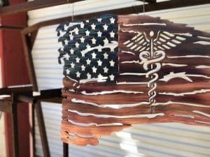 The New Battlefield Tattered Flag metal art depicts a ragged version of the American flag with the medical caduceus symbol in the flag